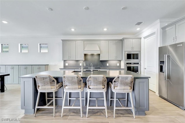 kitchen with gray cabinets, appliances with stainless steel finishes, premium range hood, a center island with sink, and visible vents