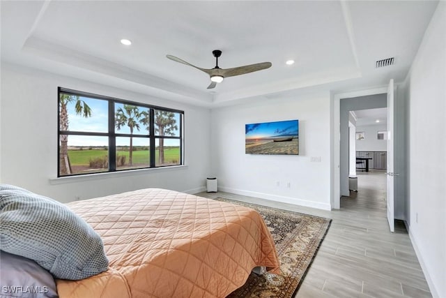 bedroom with baseboards, visible vents, light wood-style flooring, and a raised ceiling