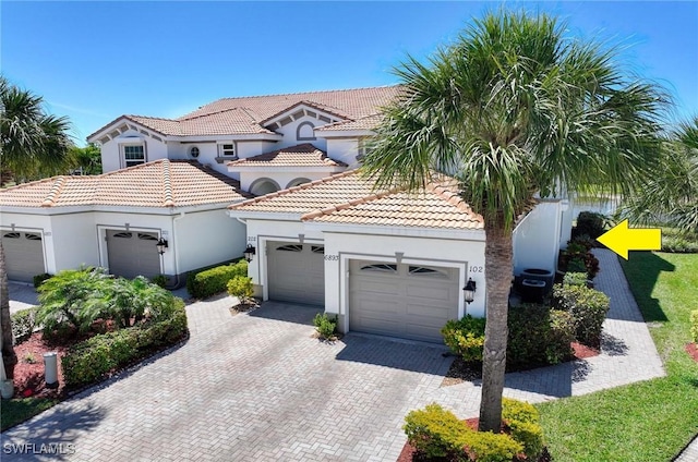 mediterranean / spanish-style house with stucco siding, decorative driveway, a tile roof, and a garage