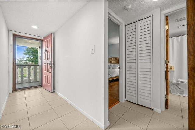 hallway with baseboards, a textured ceiling, and light tile patterned flooring