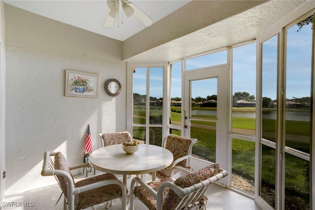 sunroom with a textured wall, a water view, and ceiling fan