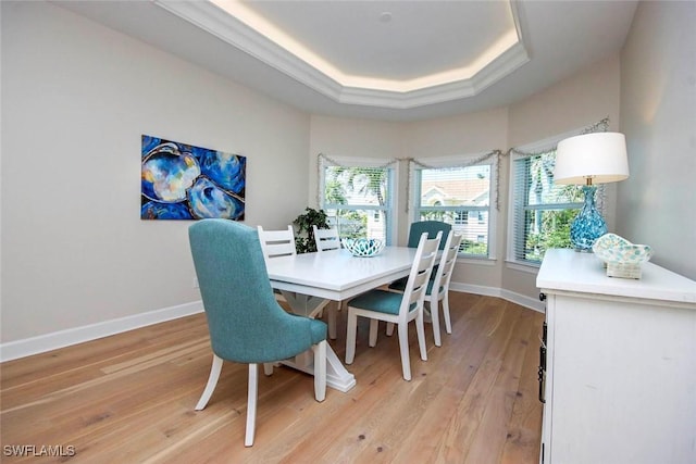 dining room with baseboards, a tray ceiling, and light wood-style flooring