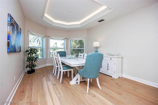 dining room featuring light wood-style flooring, a tray ceiling, baseboards, and visible vents