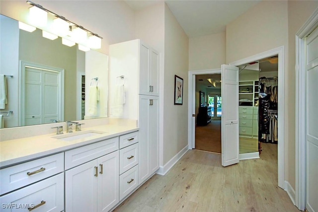 bathroom with baseboards, wood finished floors, a spacious closet, and vanity