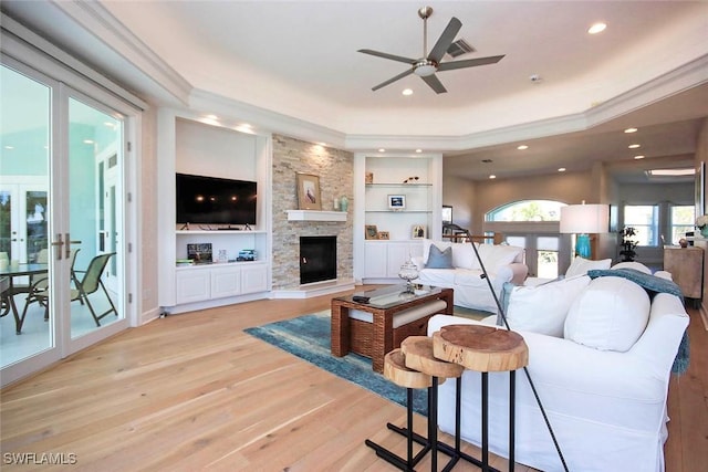 living room featuring crown molding, ceiling fan, built in shelves, a raised ceiling, and light wood-type flooring