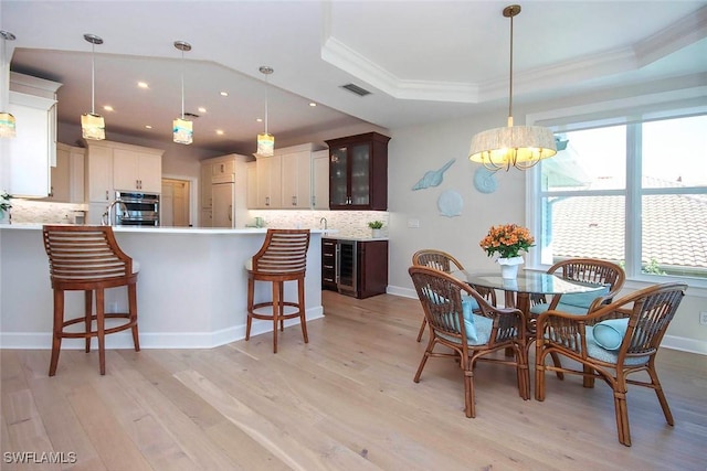dining area with a tray ceiling, crown molding, light wood-type flooring, a chandelier, and visible vents