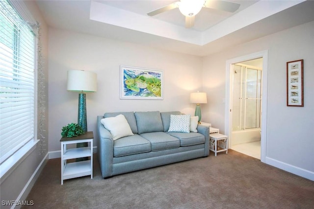 carpeted living area featuring a ceiling fan, a tray ceiling, and baseboards
