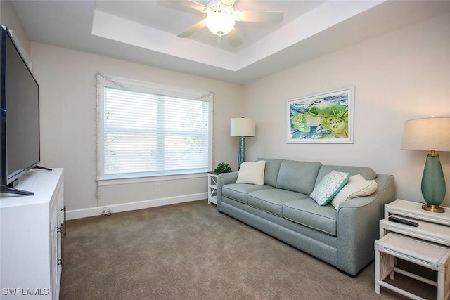 carpeted living room with a raised ceiling, baseboards, and ceiling fan