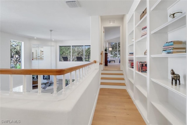 hallway featuring light wood finished floors, visible vents, and plenty of natural light