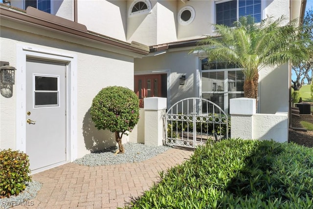 view of exterior entry with stucco siding and a gate