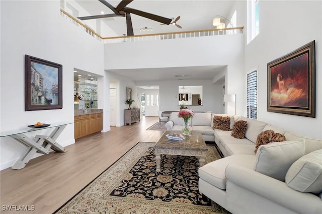living room featuring light wood finished floors, ceiling fan, baseboards, and a towering ceiling