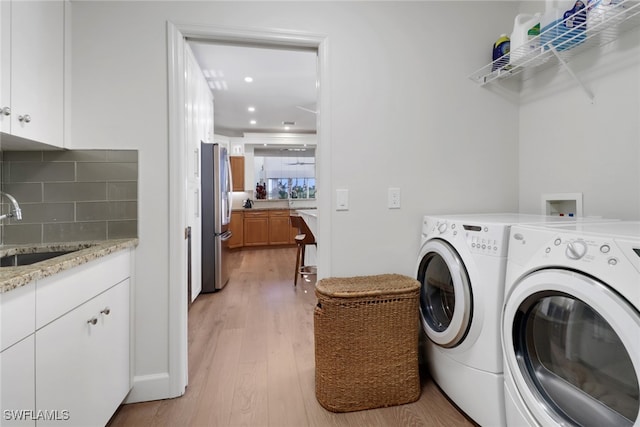 laundry room featuring light wood finished floors, washing machine and clothes dryer, a sink, and cabinet space