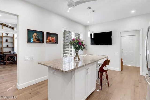 kitchen featuring a center island, baseboards, light wood-style floors, and light stone countertops