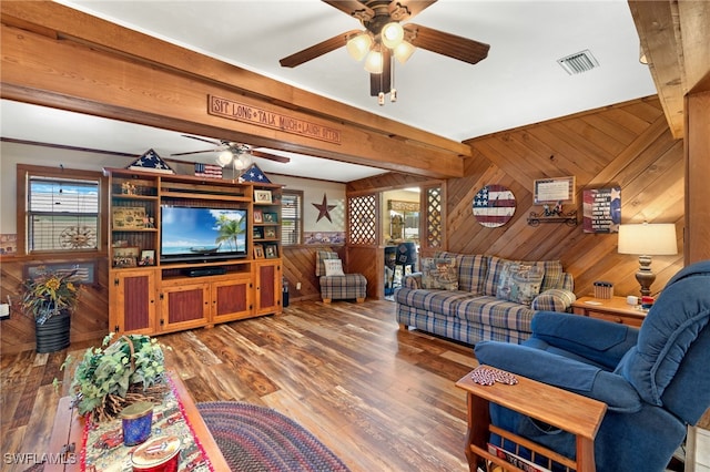 living area featuring beam ceiling, wood finished floors, wood walls, and a ceiling fan