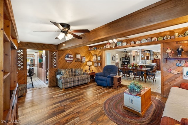 living room featuring wood finished floors, beam ceiling, wooden walls, and ceiling fan