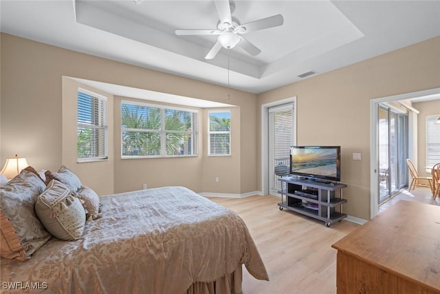 bedroom featuring baseboards, a raised ceiling, ceiling fan, light wood-style flooring, and visible vents