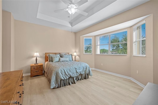 bedroom featuring baseboards, a tray ceiling, multiple windows, and wood finished floors