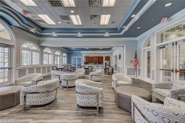 living room featuring a raised ceiling, wood finished floors, crown molding, and visible vents