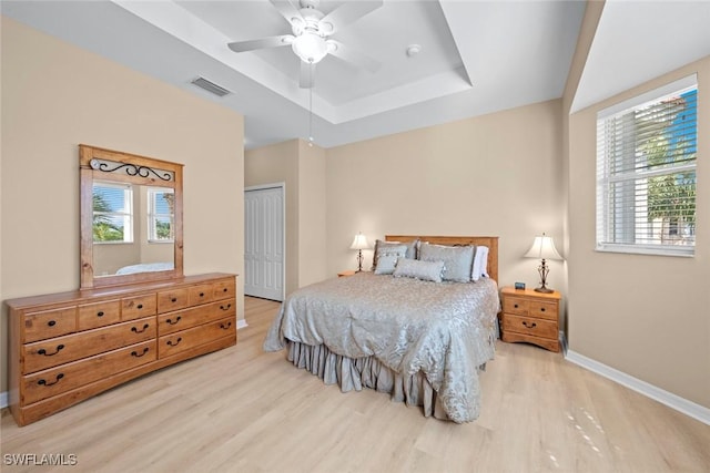 bedroom with wood finished floors, a tray ceiling, multiple windows, and visible vents