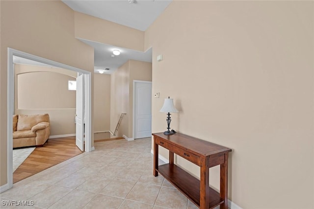 hallway featuring baseboards, an upstairs landing, and light tile patterned floors