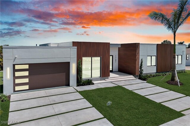modern home featuring a garage, driveway, stucco siding, and a lawn