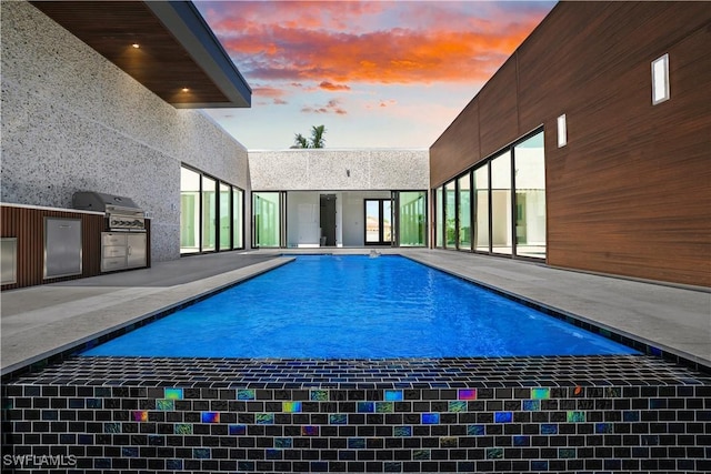pool at dusk with exterior kitchen, grilling area, a patio area, and an outdoor pool