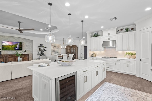 9476 Livorno Ct, Naples, FL 34119 - kitchen with beverage cooler, under cabinet range hood, cooktop, ornamental molding, and light countertops
