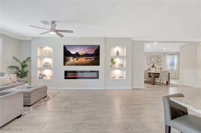living area with visible vents, ornamental molding, built in features, a glass covered fireplace, and a ceiling fan