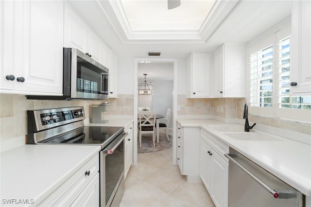 383 Harbour Dr Unit 209, Naples, FL 34103 - kitchen with stainless steel appliances, a tray ceiling, white cabinetry, a sink, and ornamental molding