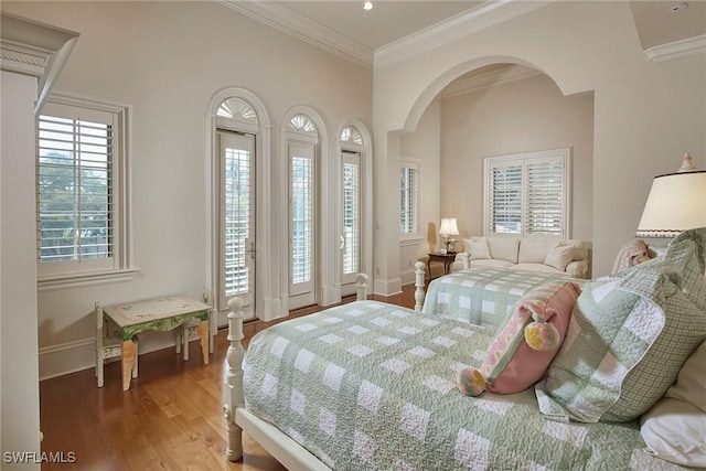 bedroom with arched walkways, crown molding, baseboards, and wood finished floors