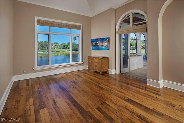 spare room with baseboards, a high ceiling, arched walkways, and hardwood / wood-style flooring