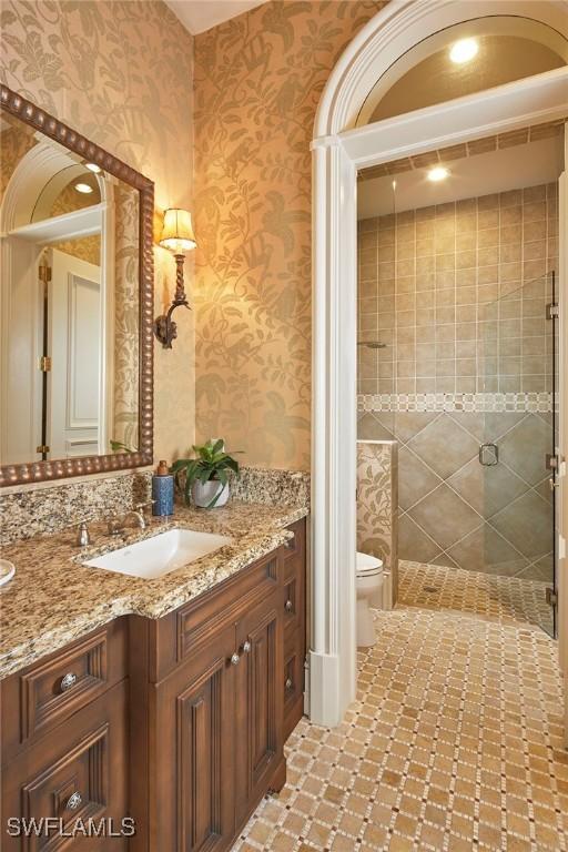 bathroom with a shower stall, wallpapered walls, toilet, and vanity