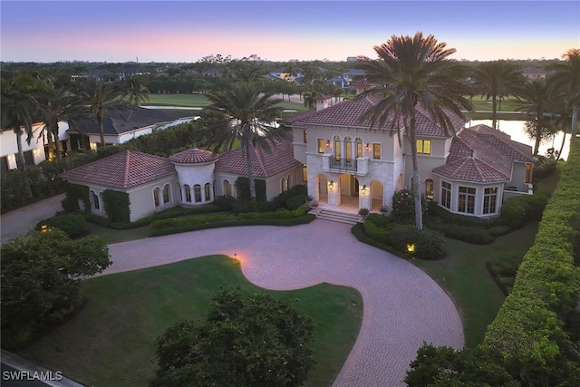 mediterranean / spanish-style house featuring a tiled roof, a balcony, curved driveway, and stucco siding