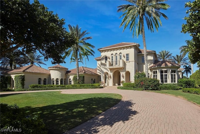 view of front of home featuring a tile roof, a balcony, curved driveway, and a front lawn
