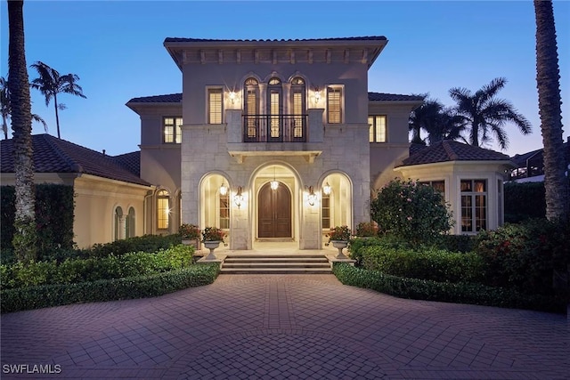 mediterranean / spanish-style house with a balcony, stone siding, and stucco siding
