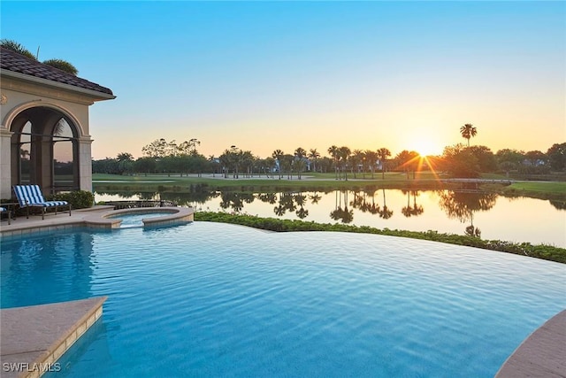 pool at dusk with a pool with connected hot tub and a water view