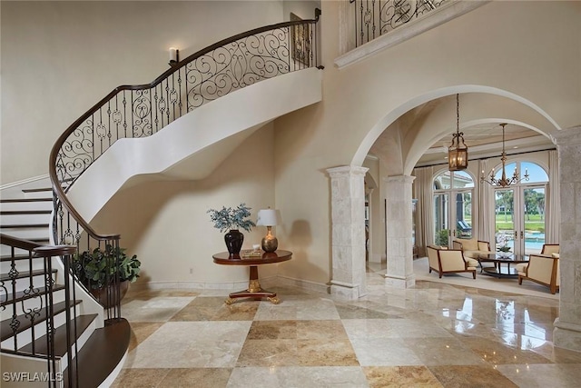 entrance foyer with stairway, decorative columns, baseboards, arched walkways, and a notable chandelier