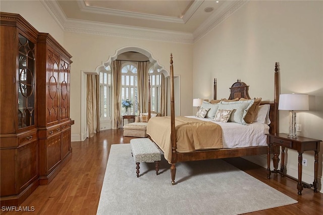 bedroom with a raised ceiling, ornamental molding, arched walkways, and wood finished floors