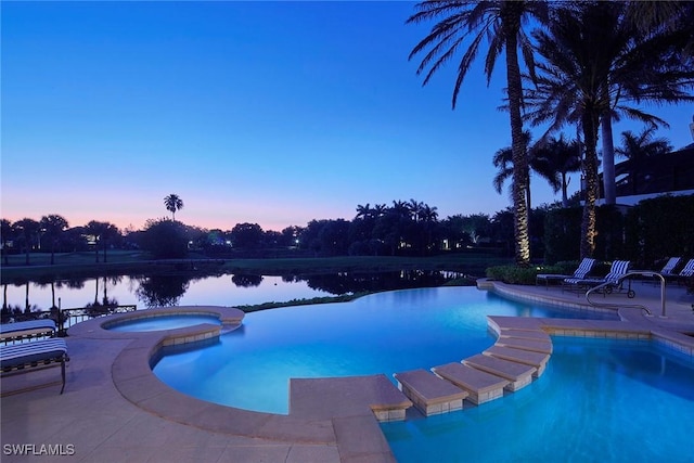 pool at dusk with a pool with connected hot tub, a water view, and a patio