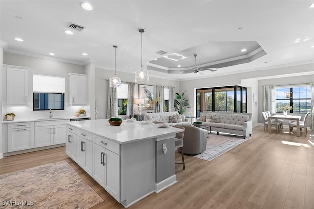 kitchen featuring crown molding, a sink, white cabinetry, a kitchen island, and light countertops