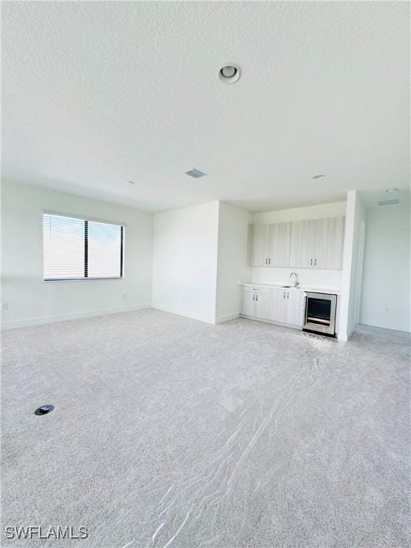 5048 Gambero Way, Ave Maria, FL 34142 - unfurnished living room featuring a textured ceiling, light colored carpet, baseboards, and beverage cooler