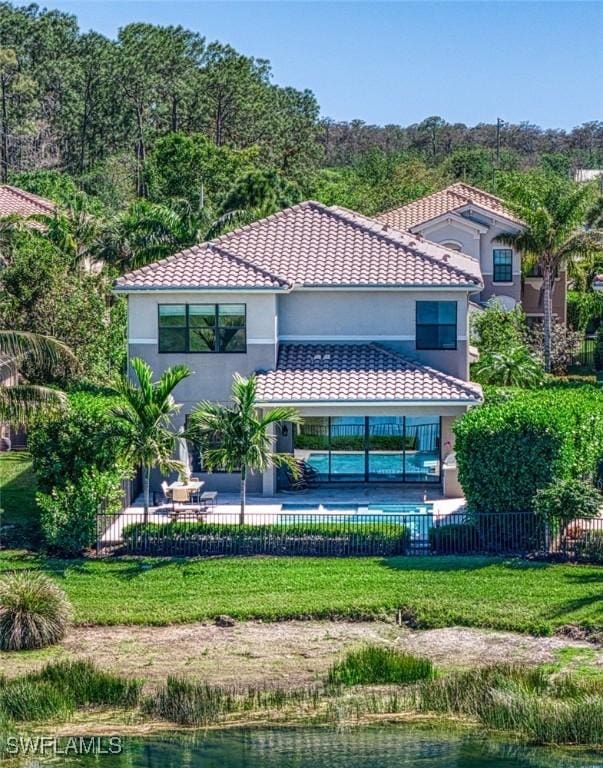 rear view of property with a lawn, fence, a tiled roof, and stucco siding