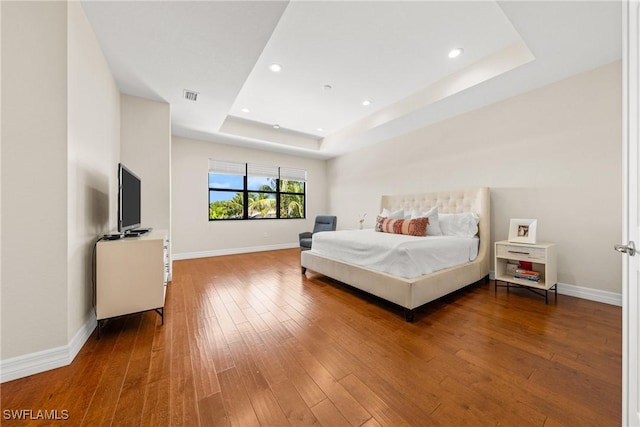 bedroom with wood-type flooring, a tray ceiling, baseboards, and visible vents