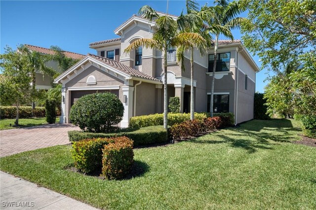 mediterranean / spanish home with stucco siding, an attached garage, a tiled roof, decorative driveway, and a front yard