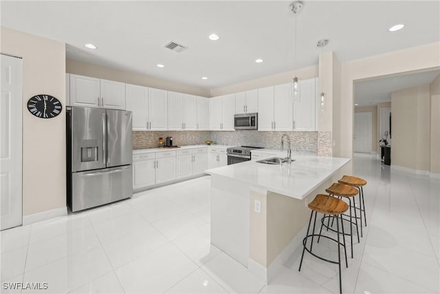 kitchen with a kitchen bar, a sink, white cabinets, a peninsula, and appliances with stainless steel finishes