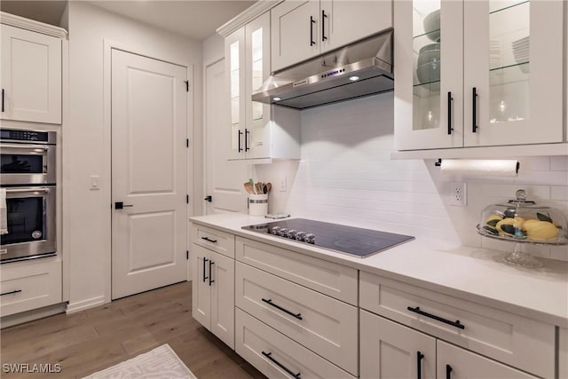 13005 Pembroke Dr, Naples, FL 34105 - kitchen with double oven, light countertops, white cabinetry, and under cabinet range hood