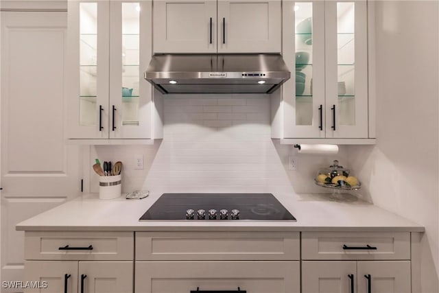 13005 Pembroke Dr, Naples, FL 34105 - kitchen with light countertops, backsplash, glass insert cabinets, black electric cooktop, and under cabinet range hood