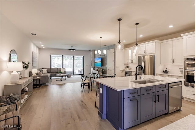 13005 Pembroke Dr, Naples, FL 34105 - kitchen featuring open floor plan, white cabinetry, stainless steel appliances, a sink, and light stone countertops
