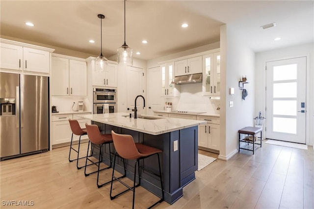 13005 Pembroke Dr, Naples, FL 34105 - kitchen with white cabinets, a breakfast bar, appliances with stainless steel finishes, under cabinet range hood, and a sink