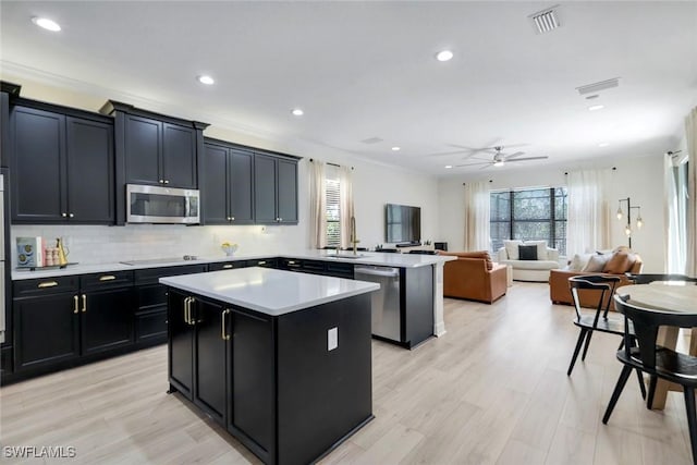 kitchen with light countertops, a sink, a kitchen island, appliances with stainless steel finishes, and dark cabinets